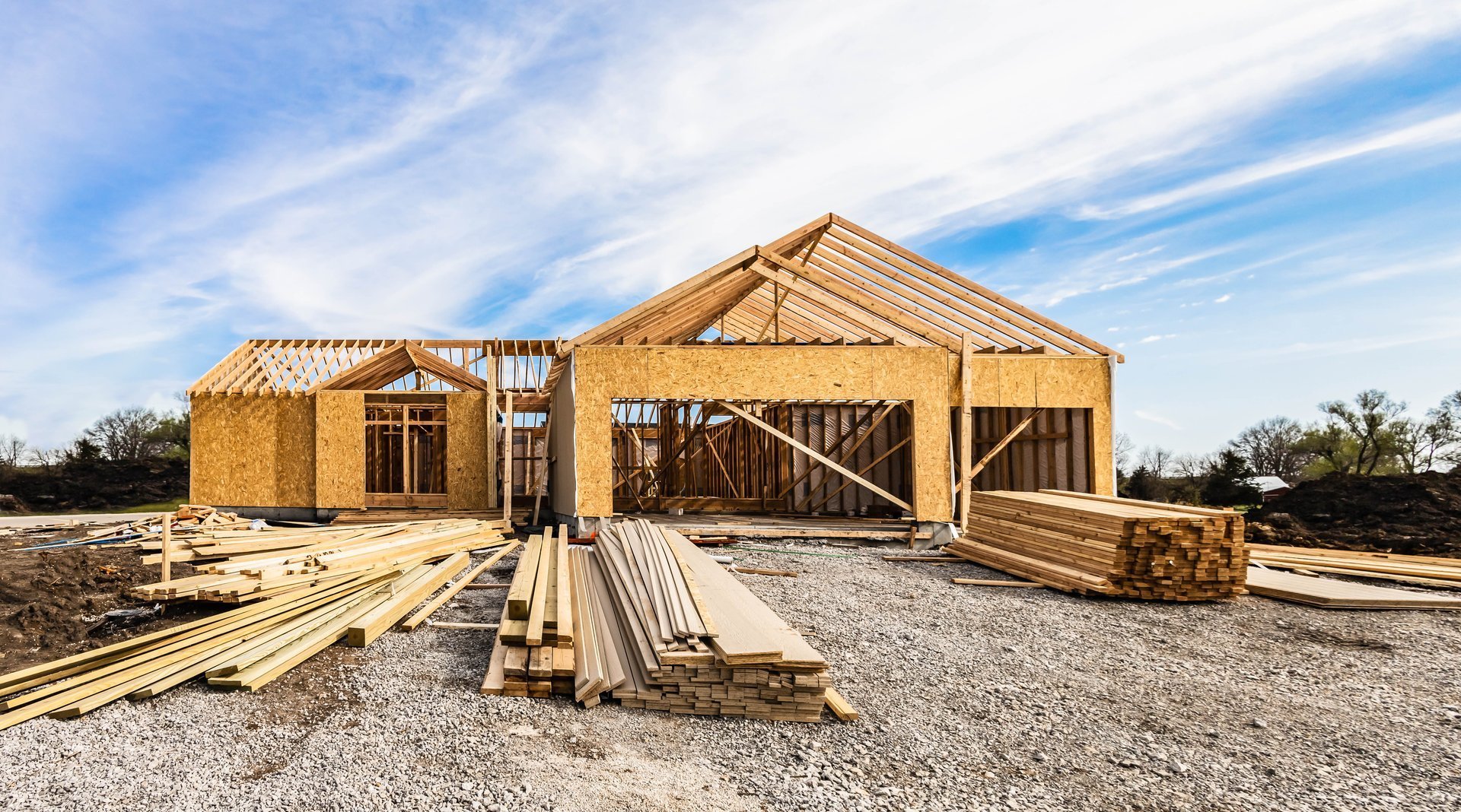New house under construction, front view with wood framing of the home exterior structure and a pile of lumber and siding planks.
