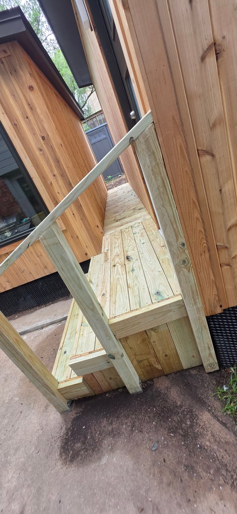 Wooden ramp with handrail leading into a modern building with wood siding and glass windows