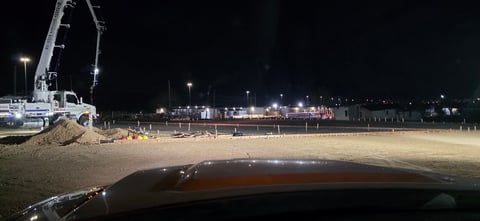 Night-time beach construction scene with heavy machinery and lit waterfront buildings in background
