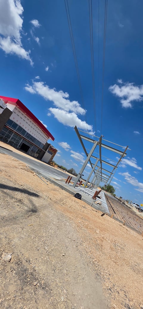 Construction site with wooden steel frame structure and red-topped industrial building under clear blue sky