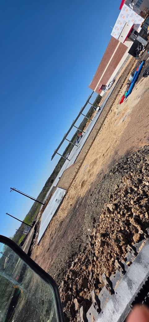 Construction site with exposed soil, metal framework, brick building, and clear blue sky