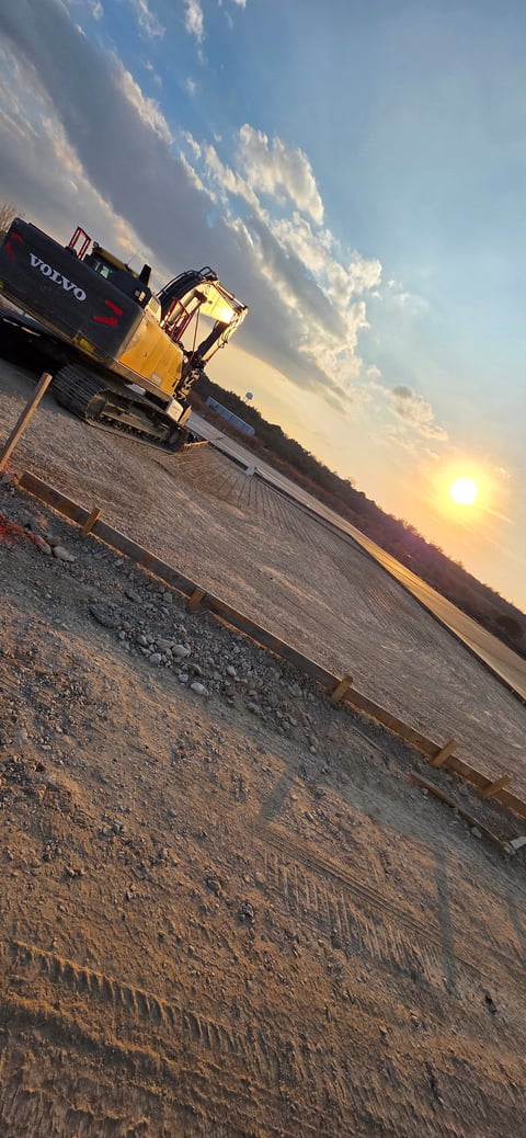 Yellow excavator on construction site at sunset with Volvo truck and dramatic cloudy sky