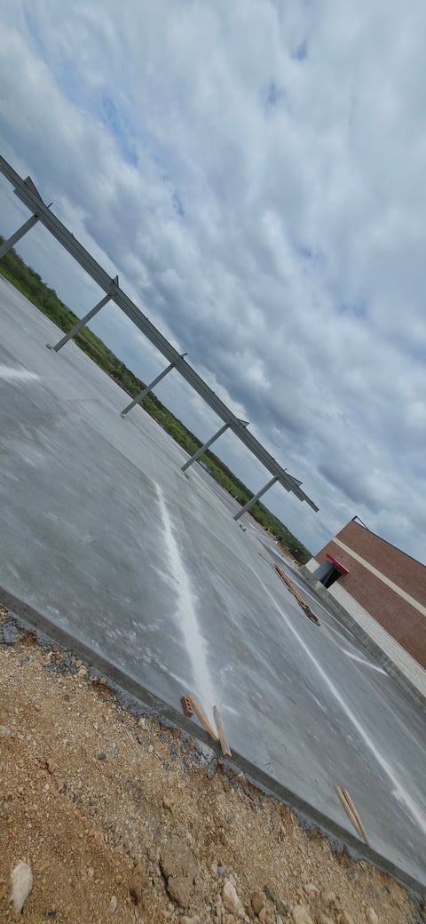 Angled view of a wooden ladder-like structure on a sandy surface with cloudy sky and water in the background